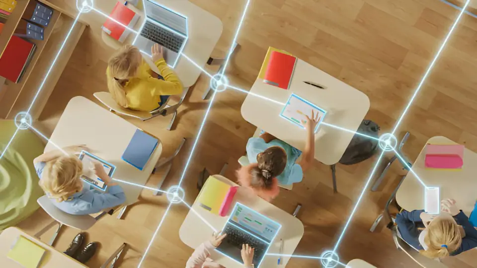 Overhead view of students at classroom desks with laptops and tablets, linked by a glowing network overlay