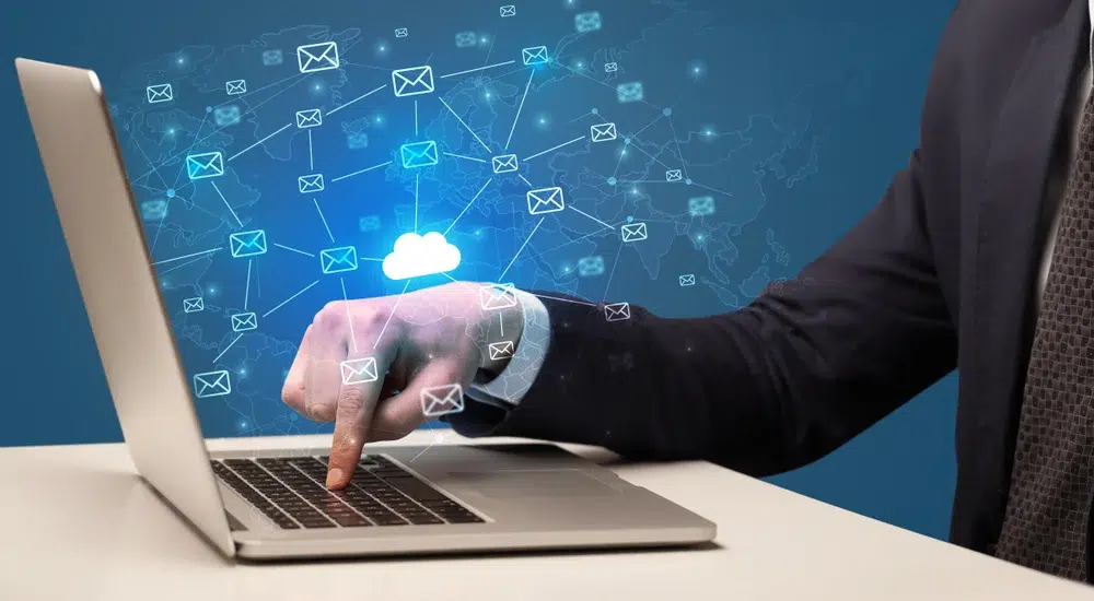 Hand typing on a laptop with email and cloud icons floating above the screen